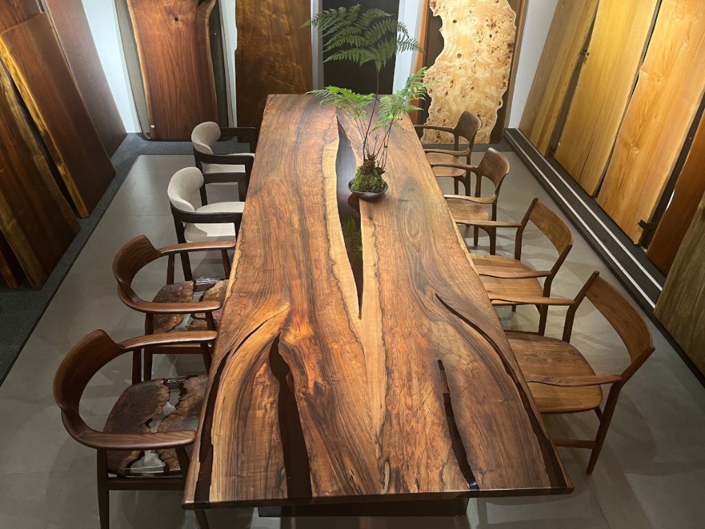 Custom handcrafted 40 by 96 inch walnut dining table with natural wood grain, modern orange leather chairs, and elegant crystal chandelier in Miami dining room